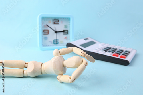 Frustrated puppet with alarm clock and calculator on blue background