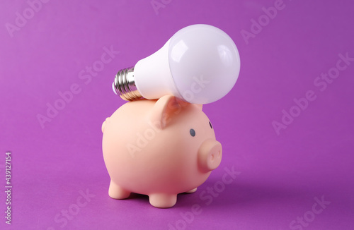 Light bulb and piggy bank on purplr background close up. Save money photo