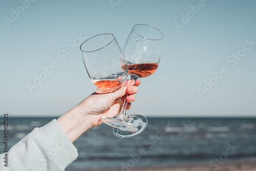 Two glasses of rose wine in female hands against the sky and seashore.