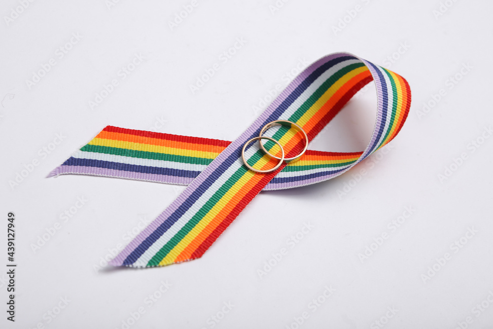 LGBT rainbow ribbon pride tape symbol with golden wedding rings on white background.
