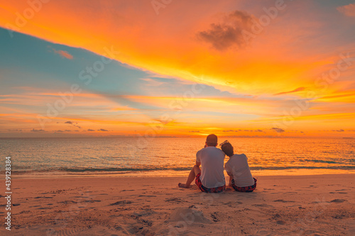 Romantic couple on the beach at colorful sunset on background. Beautiful tropical sunset scenery, romance couple sitting and watching the sunset sea and sky, horizon. Travel, honeymoon destination © icemanphotos