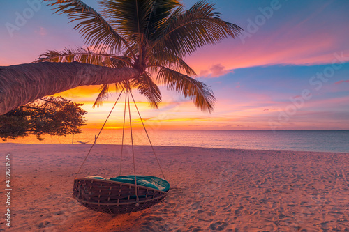 Tropical sunset beach background as summer coast landscape panorama with beach swing or hammock and white sand and calm sea beach horizon. Perfect beach resort hotel vacation or summer holiday scenery