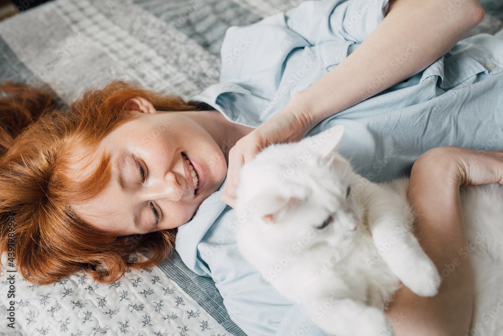 Woman embracing with her favourite white cat while laying at the bed Woman embracing with her favourite white cat while laying at the bed