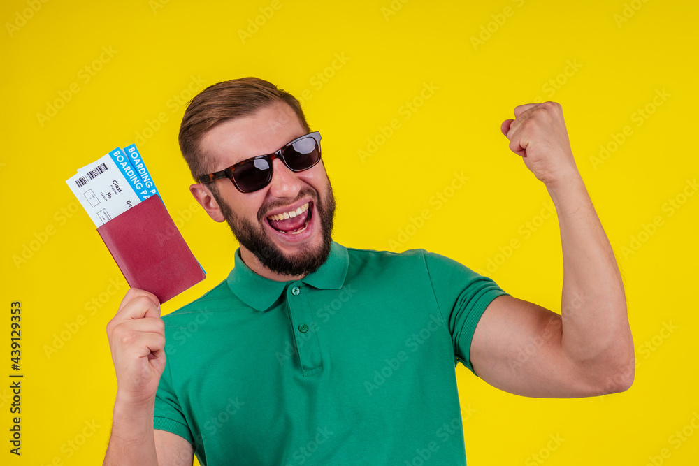 ortrait of a happy young man in sunglasses and green t-shirt holding passport isolated over yellow background ortrait of a happy young man in sunglasses and green t-shirt holding passport isolated over yellow background