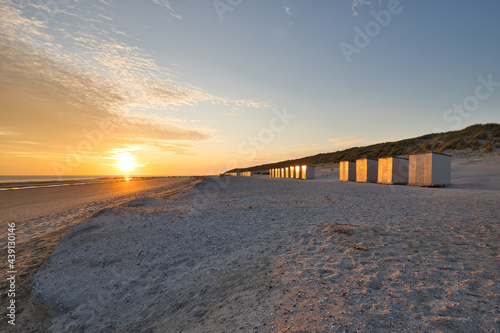 Horizontal view on a beach with a row of beach cabins at sunset in spring. North sea beach with dunes in Zeeland on a sunny day. Copy space.