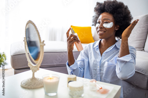 Hairstyling. Smiling Black Woman Applying Texturising Spray To Her Beautiful Curly Hair At Home, Getting Ready To Go Out, Copy Space. Young woman applying oil onto hair in living room photo