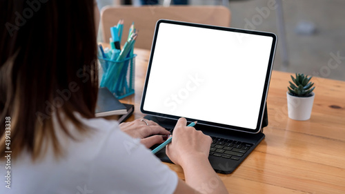 Fotografie Back view of woman holding pencil typing at keyboard tablet blank white screen at the office