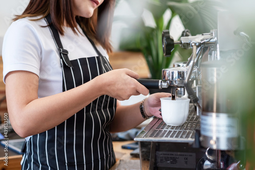 Close-up of a woman in an apron making coffee from a coffee machine at a café.