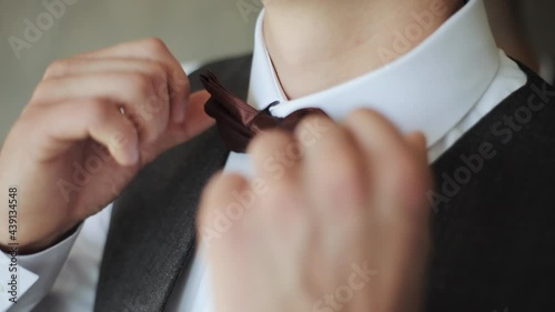Close-up of man adjusting bow tie. Attractive man epicly adjusts bow tie on suit. Man straightens bow-tie. Success style confidence establishment luxury life concept. photo