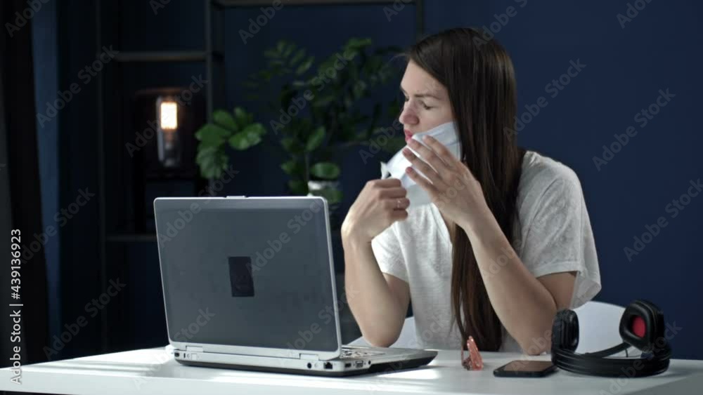 Office work during the coronavirus epidemic. Tired young business woman takes off her glasses, medical mask and closes her laptop at the end of the working day.