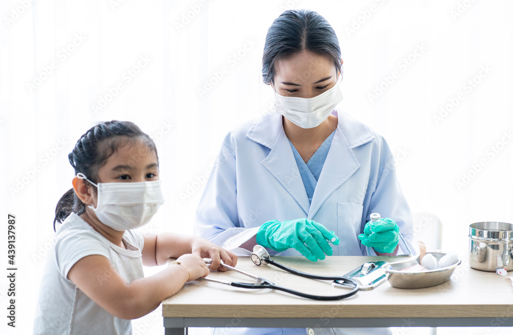 An Asian female doctor sits and examines a young girl's temperature in a clinic.