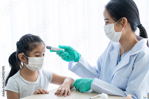 Obraz na płótnie An Asian female doctor sits and examines a young girl's temperature in a clinic. w salonie