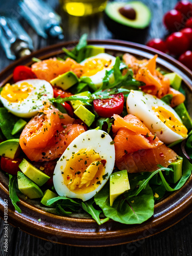 Salmon salad - smoked salmon, hard boiled eggs, avocado and green vegetables on wooden table
