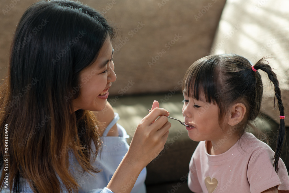 Young Asian woman feeding her younger sister with spoon of tasty cake Young Asian woman feeding her younger sister with spoon of tasty cake