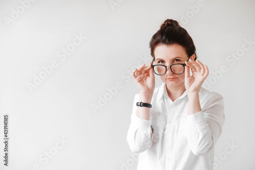 Portrait of a serious beautiful woman in optical glasses and a white shirt on a white background. Copy, empty space for text