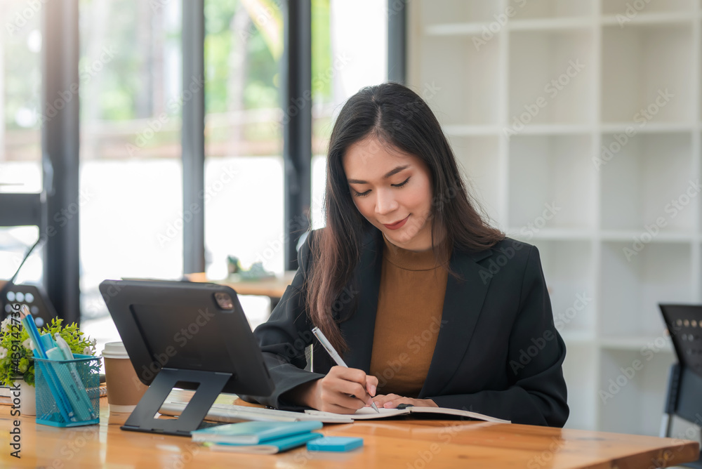 Asian businesswoman holding a pen and tablet taking notes on her desk. Asian businesswoman holding a pen and tablet taking notes on her desk.