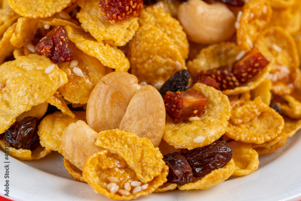Cornflakes honey caramel homemade with grains, currant, cashew nut, dried strawberries and white sesame healthy food snack on a white plate close up and Macro copy space. Cornflakes honey caramel homemade with grains, currant, cashew nut, dried strawberries and white sesame healthy food snack on a white plate close up and Macro copy space.