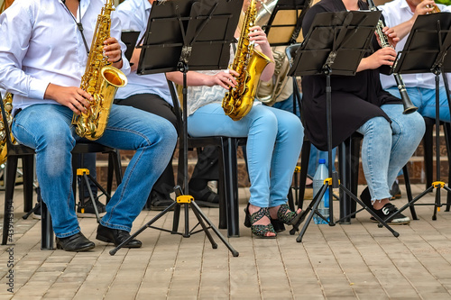 Canvas Print view of a group of people from a musical brass band who are sitting on chairs and playing music, jazz on golden copper pipes, sitting outside in the open air