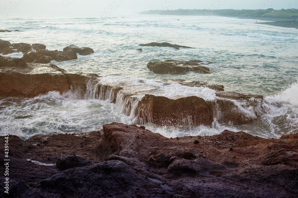 Water streaming down the rocks of the sharp reef on the ocean shore.