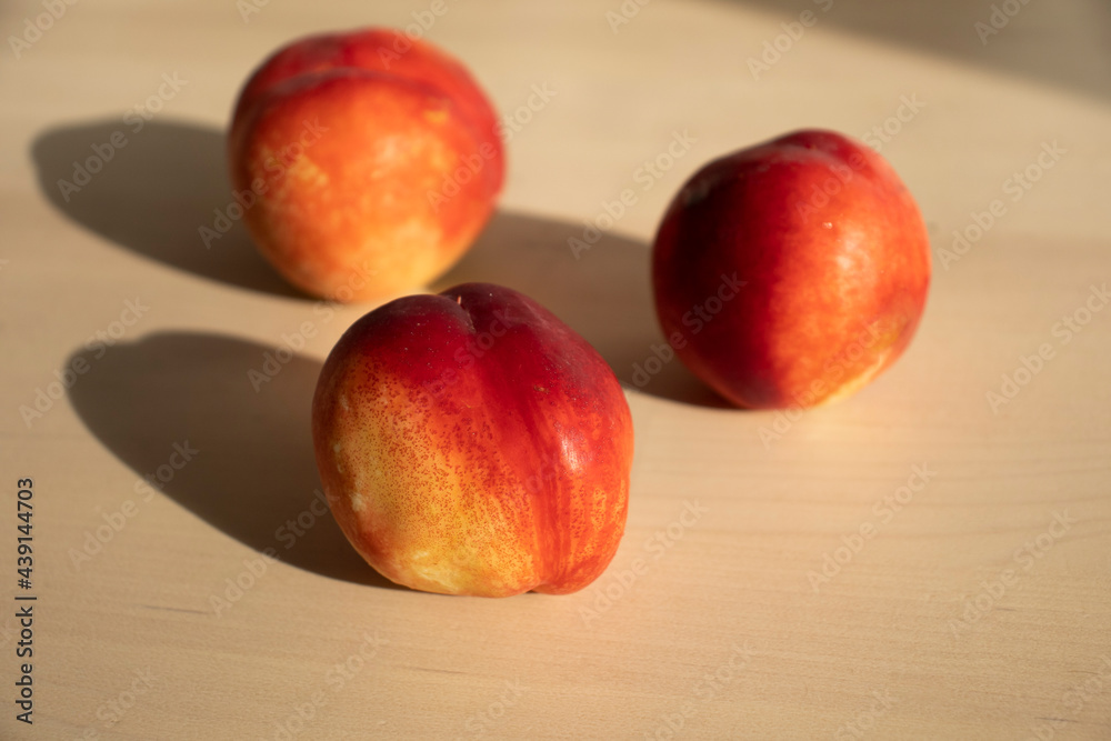 three ripe nectarines, peaches, lie on the light surface of a wooden table in the apartment. A charge of vivacity, vitamins, ripe fruits. Growing nectarine, pesticides three ripe nectarines, peaches, lie on the light surface of a wooden table in the apartment. A charge of vivacity, vitamins, ripe fruits. Growing nectarine, pesticides