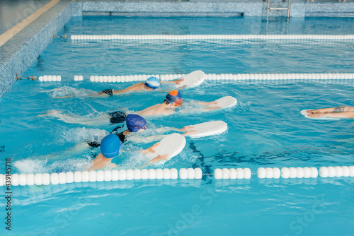 A group of boys and girls train and learn to swim in the pool with an instructor. Development of children s sports.