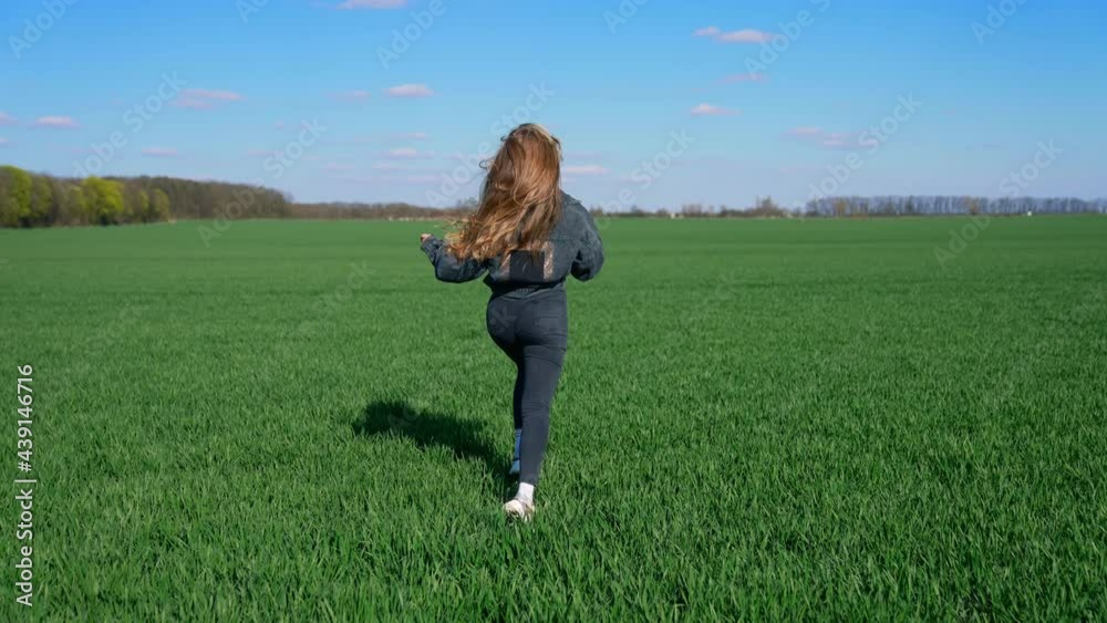 Young woman in denim suit runs on field. Happy beautiful girl is running outdoors in bright spring day. Rear view. Young woman in denim suit runs on field. Happy beautiful girl is running outdoors in bright spring day. Rear view.