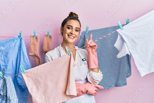 Beautiful brunette young woman washing clothes at clothesline with a big smile on face, pointing with hand and finger to the side looking at the camera.
