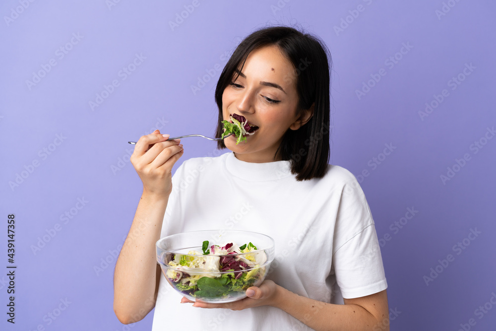 Young caucasian woman isolated on purple background holding a bowl of salad and looking at it with happy expression Young caucasian woman isolated on purple background holding a bowl of salad and looking at it with happy expression