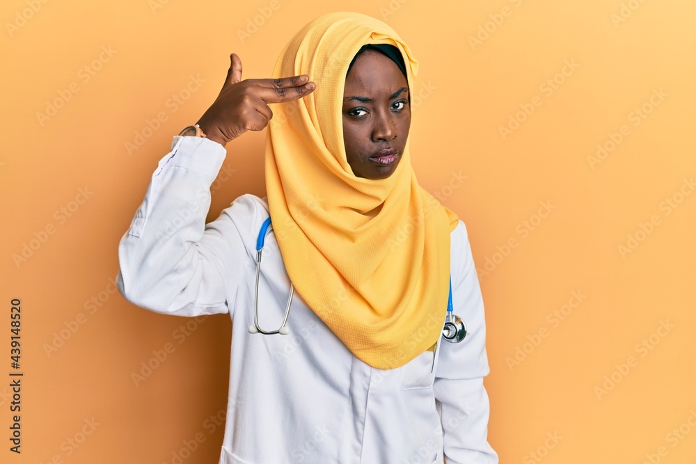 Beautiful african young woman wearing doctor uniform and hijab shooting and killing oneself pointing hand and fingers to head like gun, suicide gesture. Beautiful african young woman wearing doctor uniform and hijab shooting and killing oneself pointing hand and fingers to head like gun, suicide gesture.