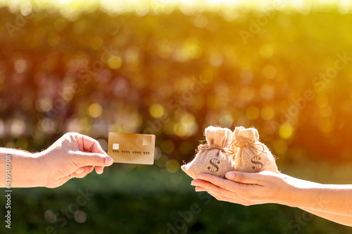 A man and a women hand holding a money bag and credit card put together in the public park, loans concept.