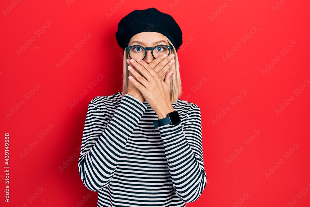Beautiful blonde woman wearing french look with beret an glasses shocked covering mouth with hands for mistake. secret concept. Beautiful blonde woman wearing french look with beret an glasses shocked covering mouth with hands for mistake. secret concept.