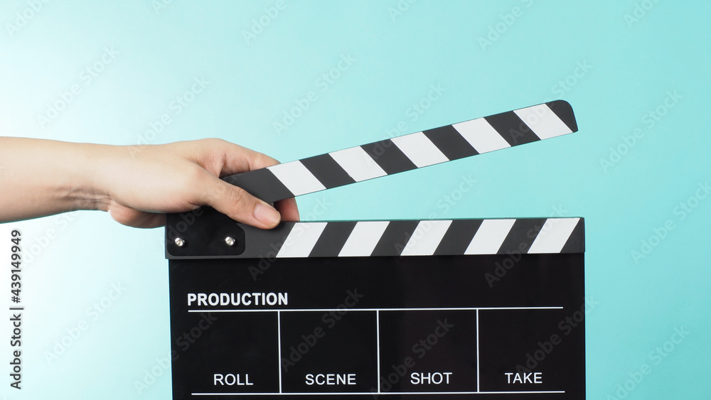 Hand is holding Black clapper board or movie slate on green or mint or Tiffany Blue background.