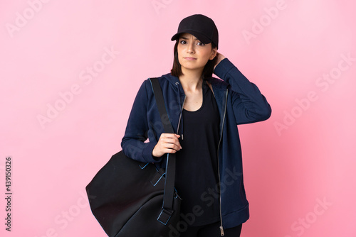 Young sport woman with sport bag isolated on pink background having doubts