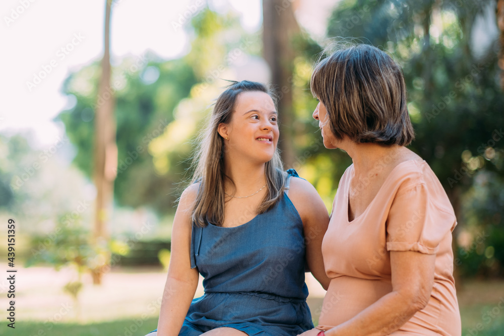 Fototapeta premium World Down Syndrome Day theme the young girl with Down syndrome with her mother’s in the park. Mother’s Day concept.