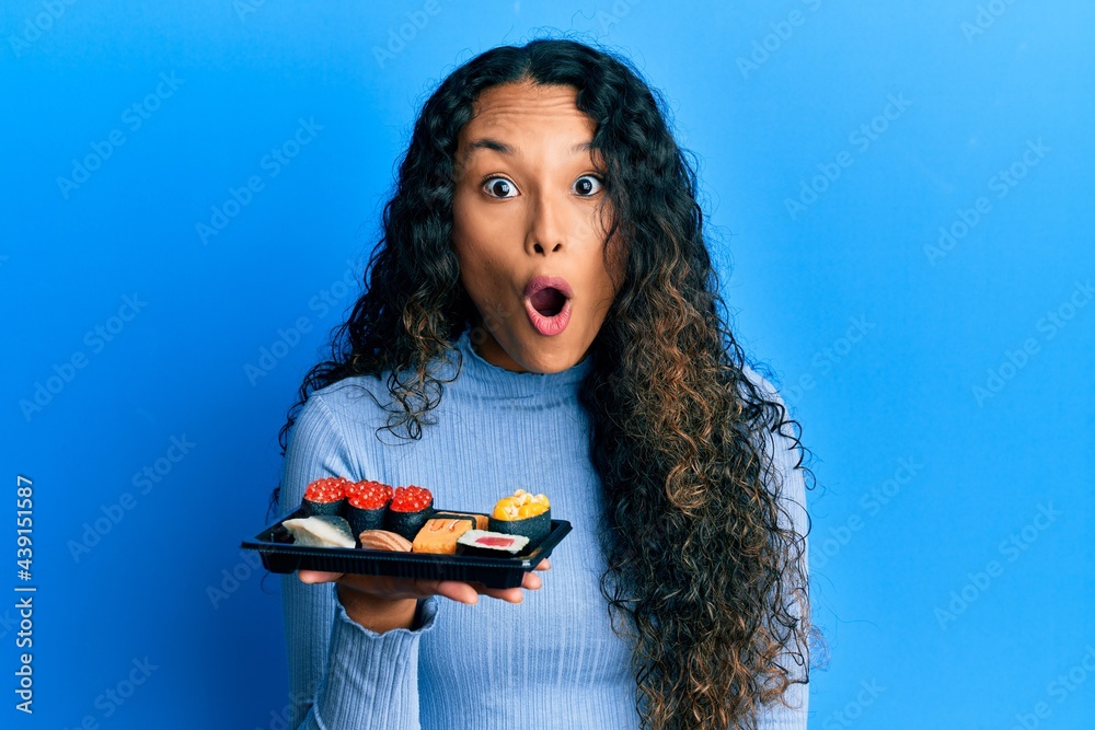 Φωτογραφία Young latin woman showing a plate of sushi scared and amazed with open mouth for