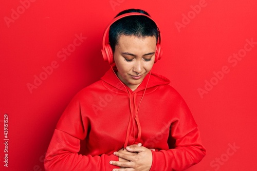 Beautiful hispanic woman with short hair listening to music using headphones with hand on stomach because indigestion, painful illness feeling unwell. ache concept. © Krakenimages.com