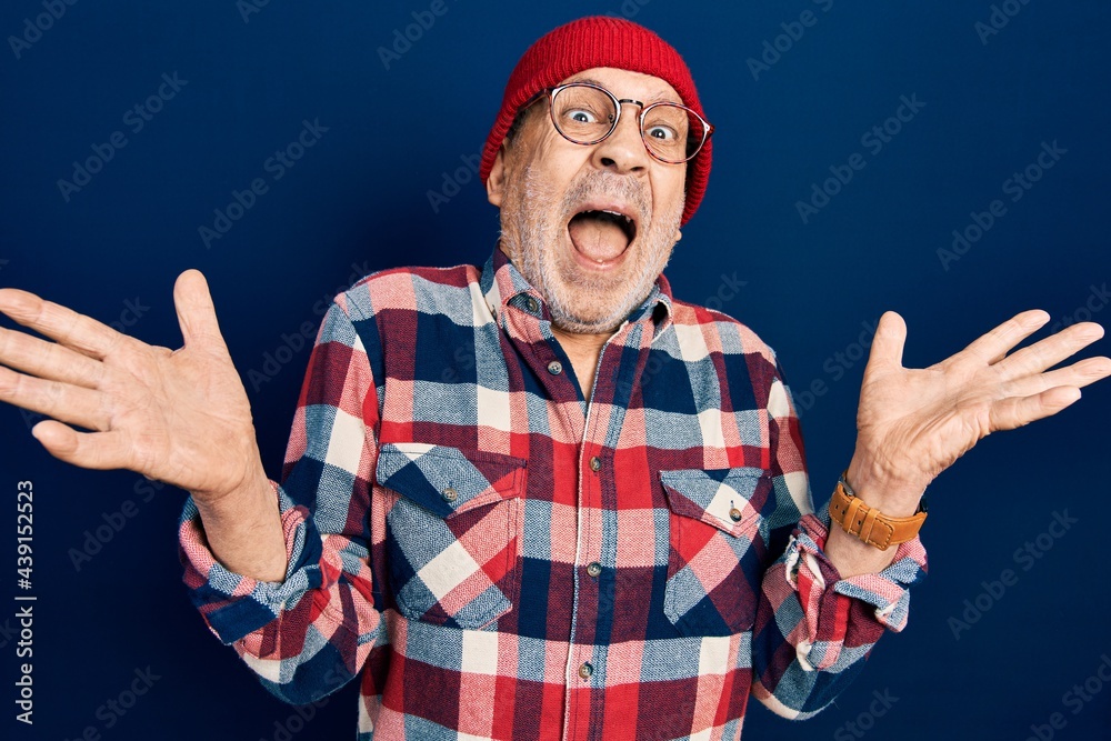 Naklejka premium Handsome mature man wearing hipster look with wool cap celebrating crazy and amazed for success with arms raised and open eyes screaming excited. winner concept