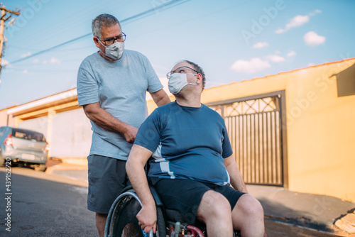 Father and son in wheelchair wearing face masks walking around town during the Covid-19 pandemic.