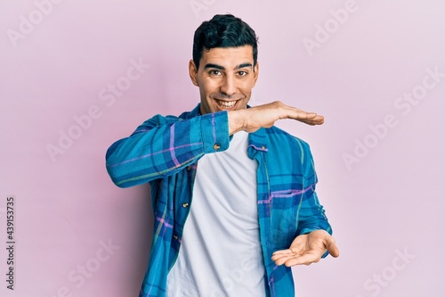 Handsome hispanic man wearing casual clothes gesturing with hands showing big and large size sign, measure symbol. smiling looking at the camera. measuring concept.