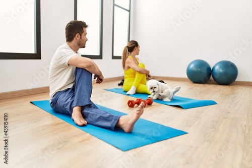 Young hispanic sporty couple stretching sitting on yoga mat at sport center.