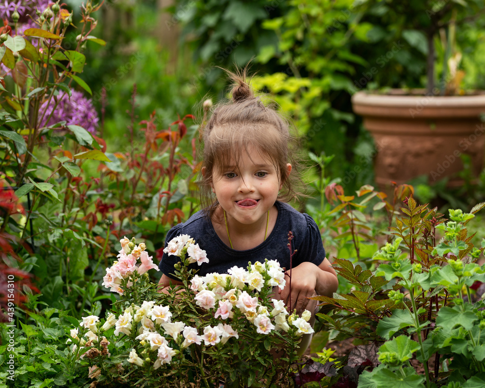 toddler girl sitting in country cottage garden full of flowers in bloom in summer