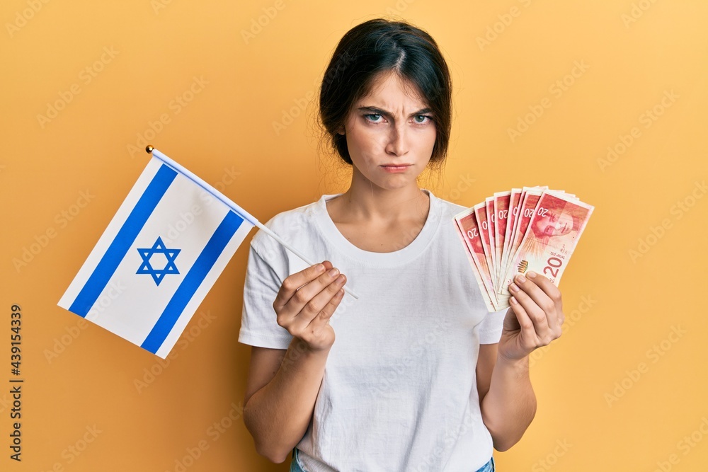 Young caucasian woman holding israel flag and shekels banknotes skeptic and nervous, frowning upset because of problem. negative person.