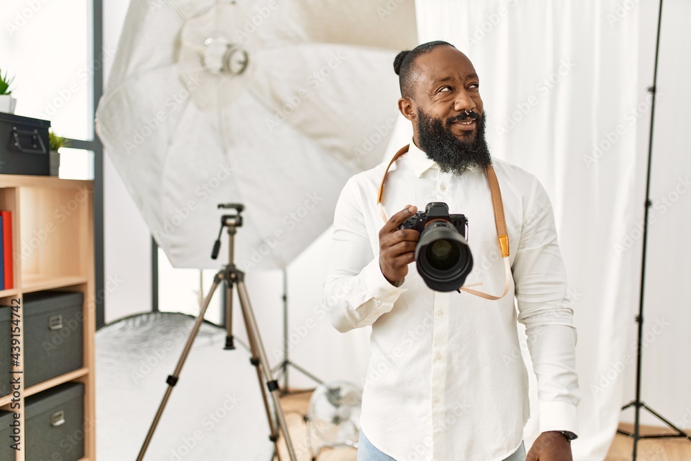 Obraz premium African american photographer man working at photography studio smiling looking to the side and staring away thinking.