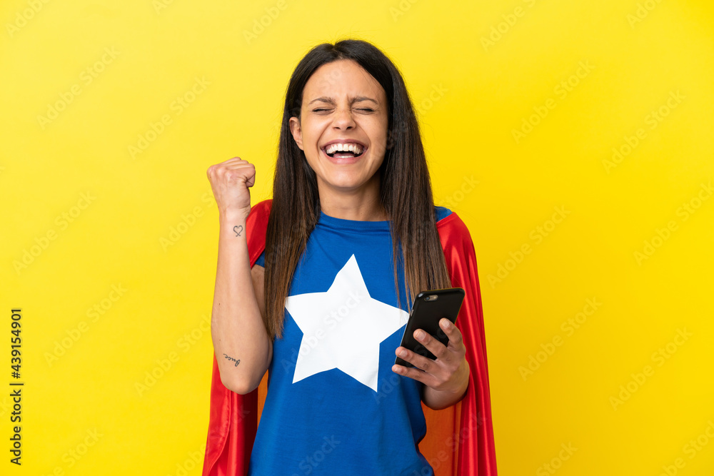 Super Hero woman isolated on yellow background using mobile phone and doing victory gesture Super Hero woman isolated on yellow background using mobile phone and doing victory gesture
