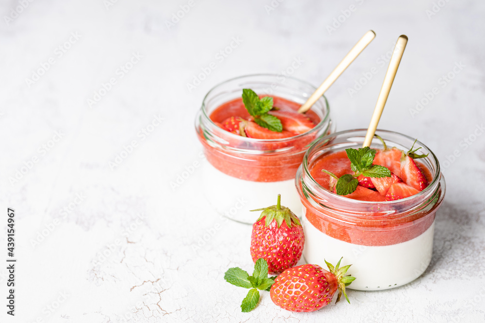 Panna cotta in glass jars with strawberry sauce and mint on white table. Panna cotta in glass jars with strawberry sauce and mint on white table.