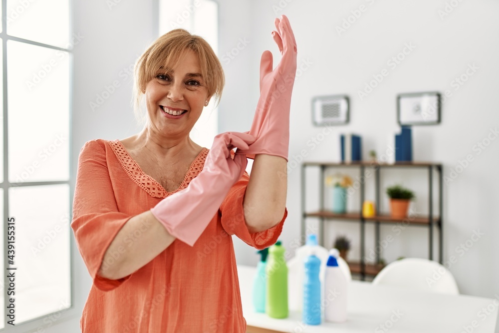 Middle age woman smiling happy put in cleaning gloves at home. Middle age woman smiling happy put in cleaning gloves at home.