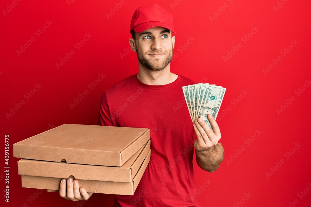 Young caucasian man holding take away food and 20 dollars smiling looking to the side and staring away thinking. Young caucasian man holding take away food and 20 dollars smiling looking to the side and staring away thinking.