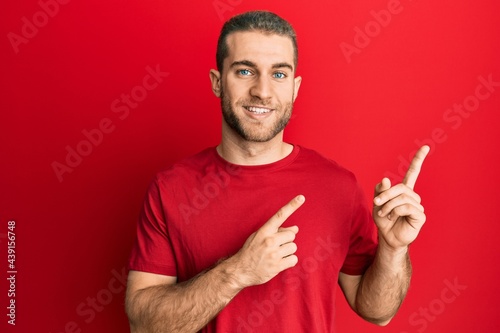 Young caucasian man wearing casual clothes smiling and looking at the camera pointing with two hands and fingers to the side.