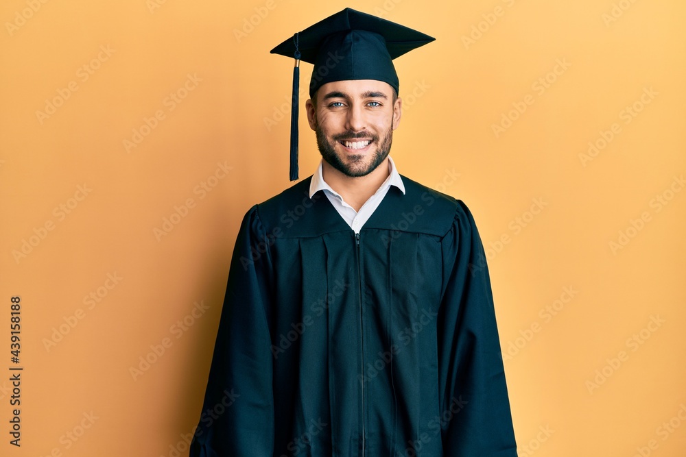 Young hispanic man wearing graduation cap and ceremony robe with a happy and cool smile on face. lucky person.