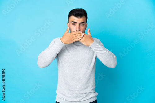 Caucasian man over isolated blue background covering mouth with hands